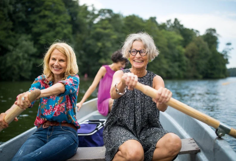 Smiling female friends rowing boat in lake